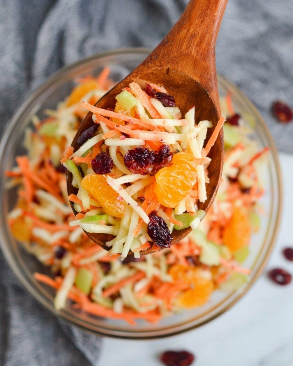 A wooden spoon holds a colorful fruit and vegetable salad made of thin orange carrot sticks as the base layer mixed with pale white apple strips and light green cucumber slices scattered inside. Bright orange mandarin segments and dark red dried cranberries are mixed on top, adding contrast to the colors. The wooden spoon is held above a clear glass bowl filled with the same mixed salad, placed on a white marbled surface with a gray cloth nearby. photo taken with an iphone --ar 4:5 --v 7
