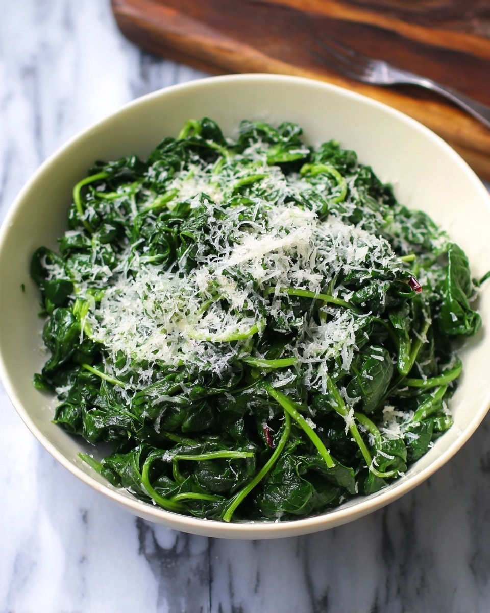 A white bowl filled with cooked dark green spinach leaves piled high, topped with a layer of finely grated white cheese scattered evenly across the surface, showing strands of bright green stems mixed in with the tender leaves, the spinach looks moist and soft. The bowl sits on a white marbled texture. Photo taken with an iphone --ar 4:5 --v 7