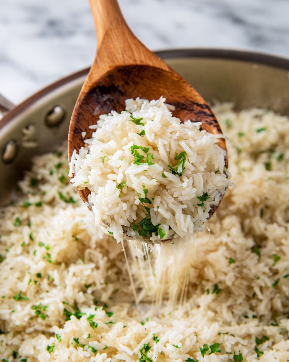 The image shows a close-up of cooked rice being lifted by a wooden spoon from a pan. The rice is white with a slight gloss, mixed with finely chopped green herbs scattered throughout. The rice texture is soft and fluffy, with some thin strands of melted cheese stretching from the pan to the spoon. The spoon holds a generous scoop of the rice, centered in the frame, with the pan visible below, filled with more of the same rice. The background features a white marbled surface that adds a clean look to the scene. photo taken with an iphone --ar 4:5 --v 7