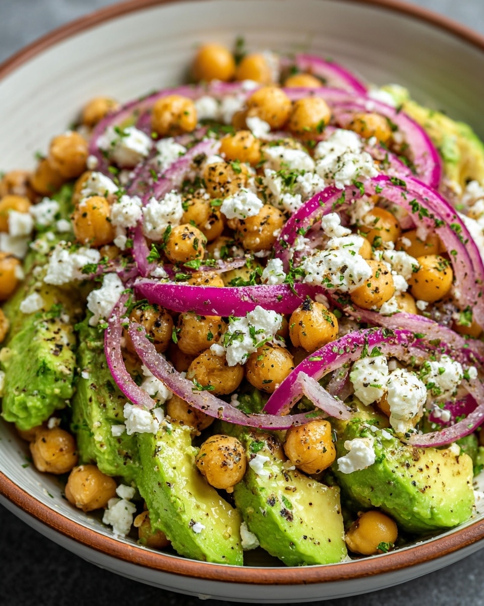 A close-up view of a salad served in a white bowl with a wooden rim, filled with three main layers. The bottom layer consists of chunks of bright green avocado with creamy texture. The middle layer is made of round, golden chickpeas sprinkled evenly throughout. The top layer has thinly sliced rings of purple-red onions, scattered dollops of crumbly white cheese, and a generous sprinkling of finely chopped green herbs and coarse black pepper, all resting on the avocado and chickpeas. The colors are vibrant and the textures range from smooth avocado to firm chickpeas and soft cheese. Photo taken with an iphone --ar 4:5 --v 7