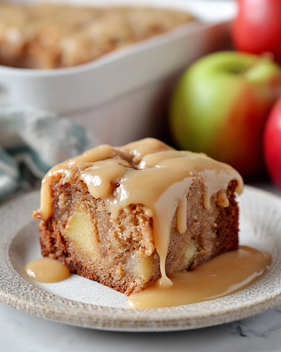 A thick slice of moist cake sits on a white plate with a textured base in light and dark brown shades, showing chunks of apple inside. The top is covered with a smooth, shiny, beige sauce that drips down the sides unevenly. In the background, out of focus, there are apples and a white baking dish with more cake on a white marbled surface. photo taken with an iphone --ar 4:5 --v 7