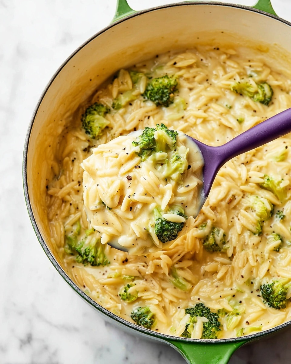 A purple spoon lifts a creamy, cheesy risotto-like dish from a white pot with a green handle, showing one main layer of soft, light yellow orzo pasta mixed with small bright green broccoli florets. The orzo appears tender and well-coated in a smooth, light yellow sauce speckled with black pepper bits. The pot rests on a white marbled surface. Photo taken with an iphone --ar 4:5 --v 7