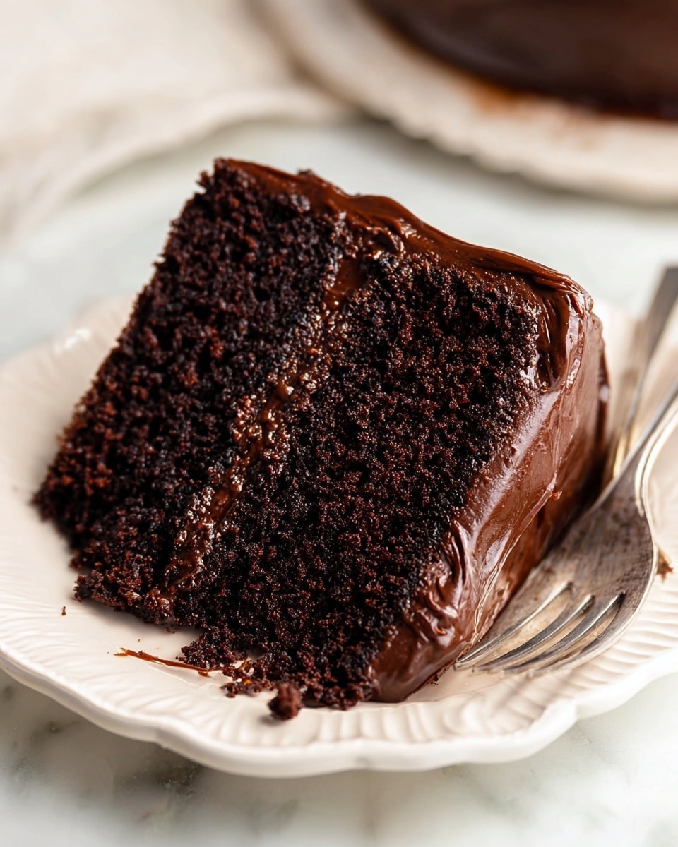 A close-up of a slice of chocolate cake on a white scalloped plate, showing two thick, soft layers of dark brown cake with a moist texture. Between and covering the cake layers is a glossy, smooth dark chocolate frosting that spreads slightly over the edges and base with visible swirls. The plate rests on a white marbled surface, with a silver fork blurred in the background. Photo taken with an iphone --ar 4:5 --v 7