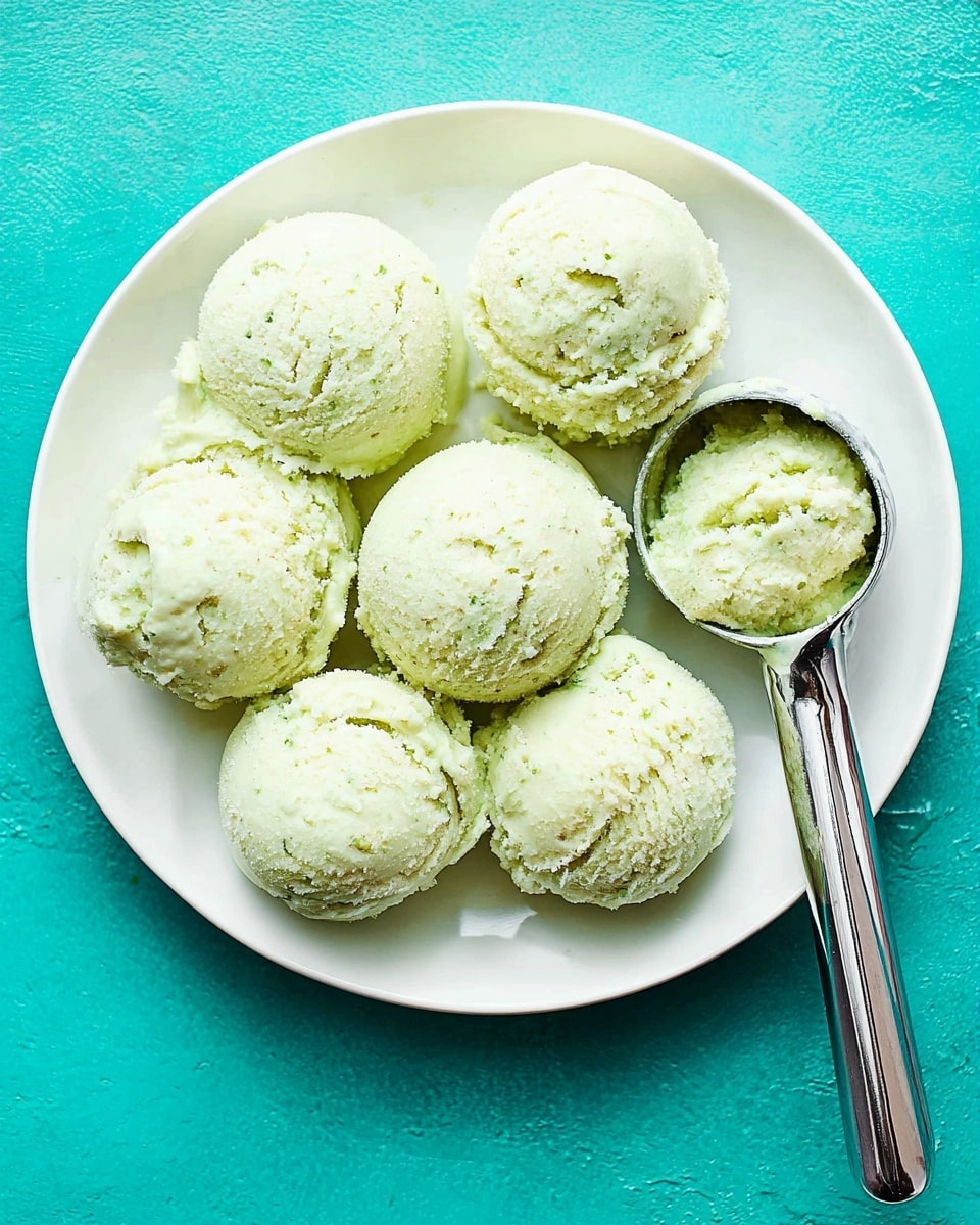 A white plate holds eight round scoops of pale green, creamy ice cream with a slightly crumbly texture, arranged close together in a neat cluster. A shiny silver ice cream scoop, filled with one of the same pale green textured scoops, rests on the right side of the plate. The plate is set on a vivid turquoise background that contrasts with the light color of the ice cream. photo taken with an iphone --ar 4:5 --v 7