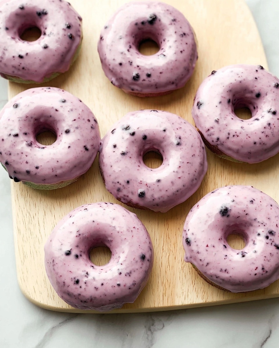 Six donuts with light purple glaze speckled with small dark purple dots cover the top of each donut. The donuts are round with a hole in the middle, and underneath the glaze, the donut base shows a faint green-gray color with some darker spots. They are arranged loosely on a light beige wooden board with a subtle grain texture, set against a white marbled surface visible at the bottom edge. The glaze appears smooth and slightly shiny, covering most of the top surface of each donut and dripping slightly on some edges. photo taken with an iphone --ar 4:5 --v 7