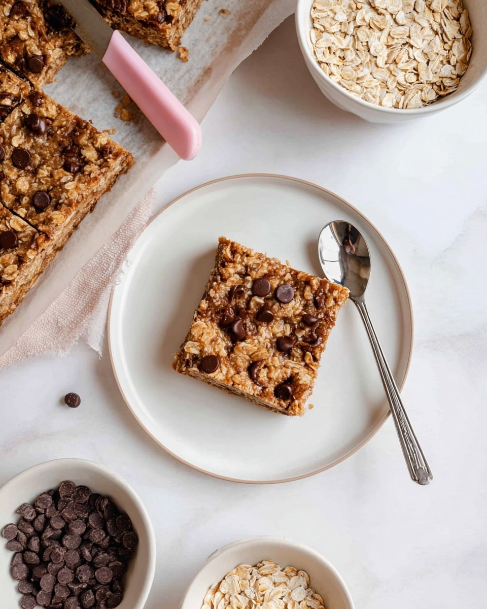 The image shows a square oat and chocolate chip bar with a rough texture and a golden brown color, sitting in the center of a white plate. The bar has visible oatmeal flakes mixed throughout and scattered dark chocolate chips on top. Next to the bar on the plate is a spoon with a silver round head and a long black handle. In the upper left corner, a tray lined with parchment paper holds similar oat bars, one cut missing with a pink-handled knife resting on the paper. Around the scene, two white bowls hold raw oats and dark chocolate chips, all placed on a white marbled surface. photo taken with an iphone --ar 4:5 --v 7