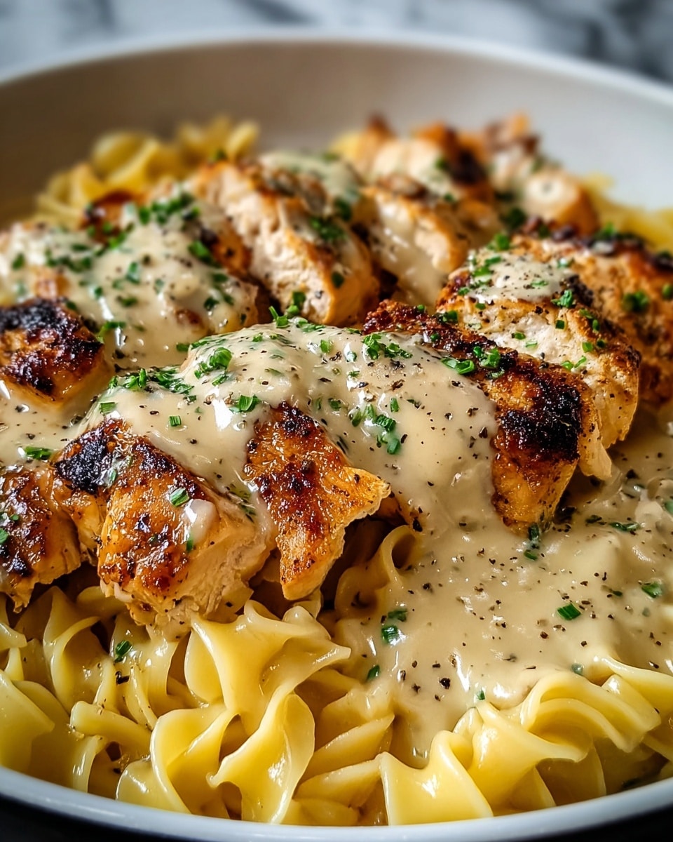 A close-up view of a dish with three layers; the bottom layer is creamy yellow twisted noodles, the middle layer consists of golden brown grilled chicken pieces with visible char marks, and the top layer is a light beige creamy sauce drizzled over the chicken, sprinkled with chopped green herbs and black pepper. The food is served in a white bowl, placed on a white marbled texture surface. photo taken with an iphone --ar 4:5 --v 7