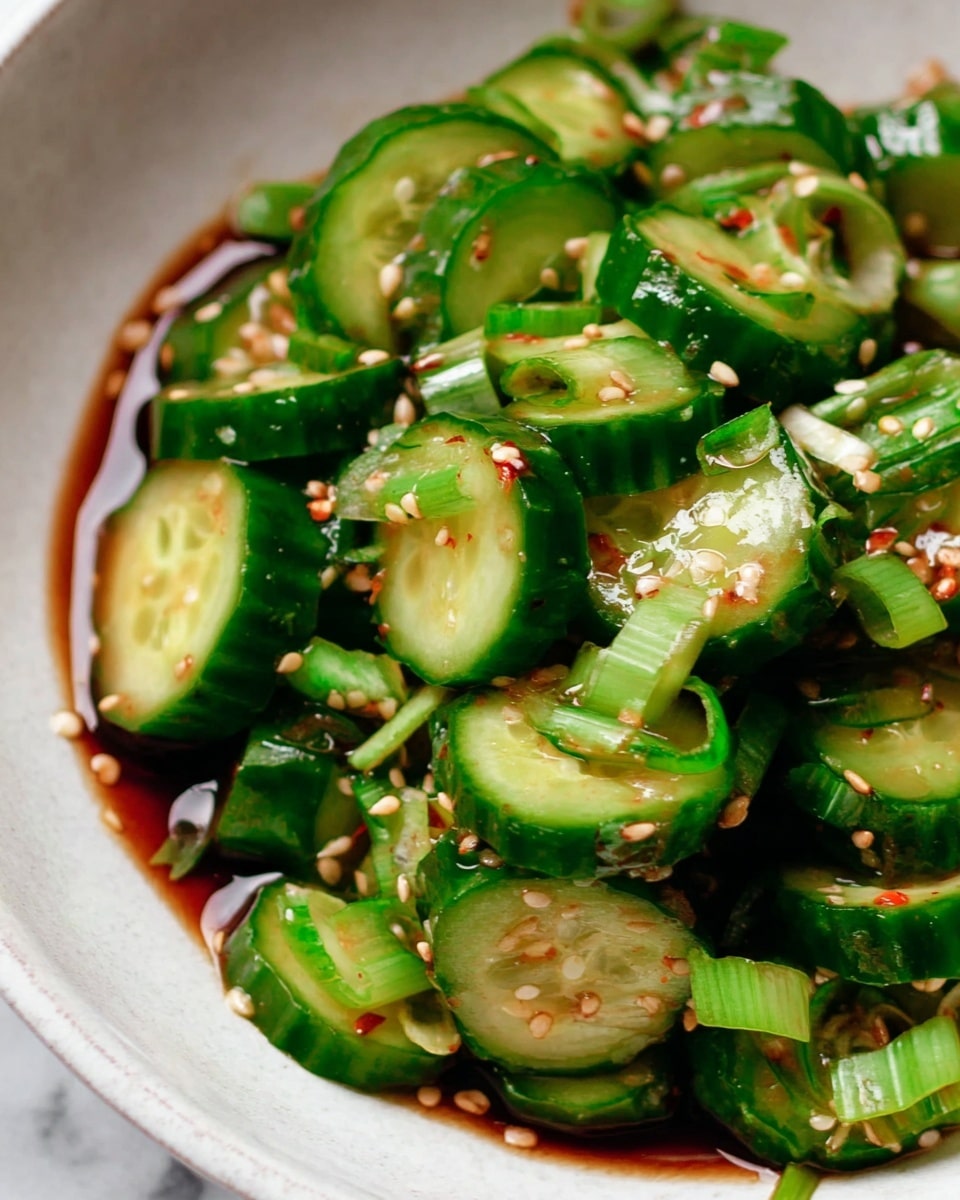 This close-up image shows a bowl filled with sliced cucumber rounds and diagonally cut green onion pieces mixed together. The cucumber slices are bright green with a shiny, wet look, layered thick and stacked in a slightly messy way. The green onions are scattered evenly throughout, adding a different texture with their light and dark green shades. The salad is sprinkled with small pale sesame seeds and tiny red chili flakes, resting in a thin, dark soy-based sauce that pools lightly at the bottom. The bowl itself is white, placed on a white marbled surface. photo taken with an iphone --ar 4:5 --v 7