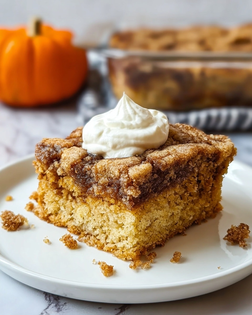 A single square slice of crumb cake with a golden-brown, crumbly texture sits on a white round plate. The cake has a marbled top layer of darker cinnamon brown swirls, with a light golden crumb below. A dollop of smooth, creamy white whipped topping is placed on the center of the cake slice. Crumbs are scattered lightly around the base on the plate. In the background, there is a glass baking dish filled with more crumb cake, and a small orange pumpkin is partially visible on a white marbled surface. photo taken with an iphone --ar 4:5 --v 7