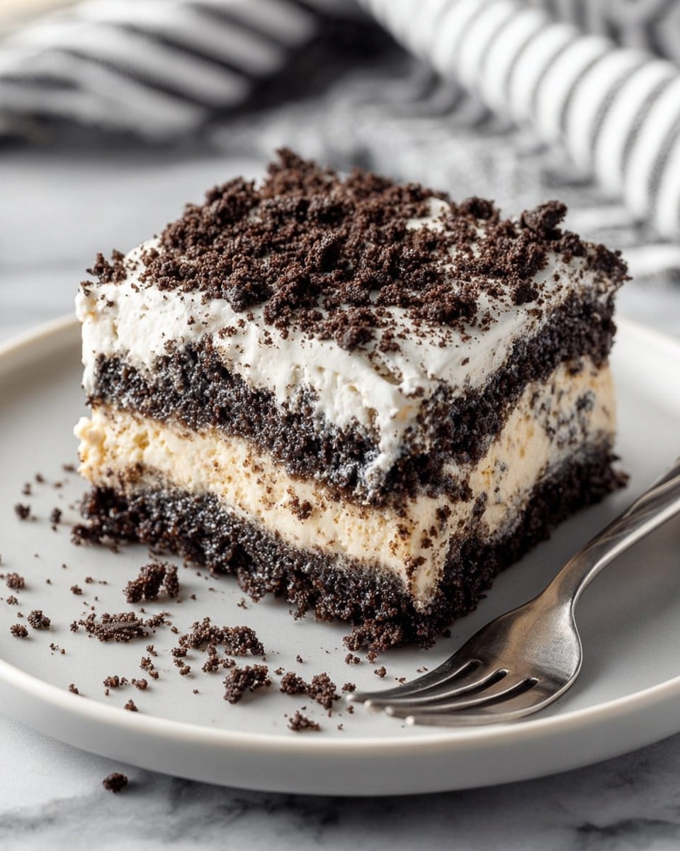 A square slice of layered dessert on a white plate shows three visible layers: the bottom layer is dark, crumbly chocolate cake, the middle layer is a thick, light beige creamy filling with bits of chocolate mixed in, and the top layer is a fluffy white cream sprinkled heavily with dark chocolate cookie crumbs. Crumbs are scattered slightly around the plate, and a silver fork rests on the right side. The plate sits on a white marbled texture with a blurred striped cloth in the background. Photo taken with an iphone --ar 4:5 --v 7