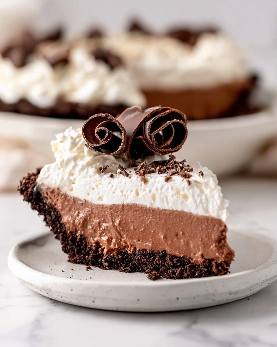 A round pie with three visible layers sits in a white pie dish on a white marbled surface. The bottom layer is a dark chocolate crumb crust, dark and crumbly. Above it is a smooth light brown chocolate mousse layer, thick and creamy. The top layer is a thick white whipped cream, swirled with soft peaks. On top, there are many dark and milk chocolate curls arranged in the center, making a textured, rich topping. Nearby, a white bowl holds more chocolate curls, and a fork rests on stacked white plates with a pink cloth nearby. Photo taken with an iphone --ar 4:5 --v 7