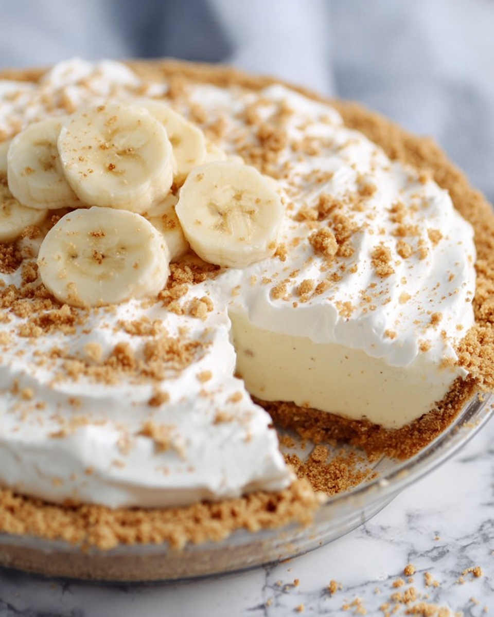 The image shows a pie with three clear layers, placed on a white marbled surface. The bottom layer is a light golden-brown crust with a slightly uneven edge. The middle layer is thick, creamy, and white, covering the entire crust smoothly. The top layer is whipped cream, fluffy and white, spread evenly with small peaks and sprinkled with crushed light brown crumbs. On the very top, there are several slices of banana arranged in a small cluster near the center. Photo taken with an iphone --ar 4:5 --v 7