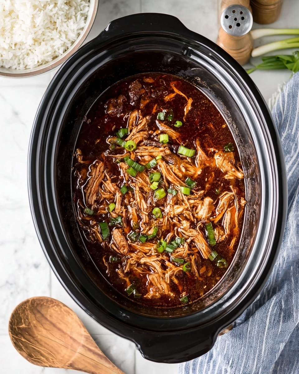 Inside a black slow cooker, there is shredded chicken mixed with a glossy dark brown sauce that looks thick and rich. Small green pieces of chopped green onions are scattered on top, adding color contrast. The slow cooker sits on a white marbled surface. To the side, part of a white bowl filled with white rice is visible, along with a wooden spoon resting on a blue and white striped cloth. There are also green onions and salt and pepper shakers in the background. Photo taken with an iphone --ar 4:5 --v 7