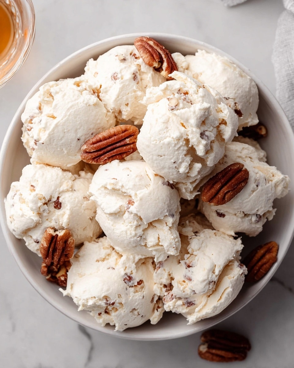 A white bowl filled with multiple large dollops of creamy, off-white, textured meringue clusters that have a slightly rough surface and small chunks of pecans visible inside and on the edges, some pecan halves are nestled in between the dollops, all placed on a white marbled surface. Photo taken with an iphone --ar 4:5 --v 7