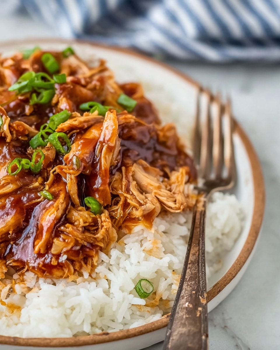 This image shows a close-up of shredded chicken coated in a thick, glossy brown sauce with small green onion pieces on top. The chicken is layered over a bed of soft, white rice on a white plate with a thin brown rim. A weathered metal fork rests on the plate, partially covered by the saucy chicken and rice. The setting includes a white marbled surface and a blurred blue and white striped cloth in the background. photo taken with an iphone --ar 4:5 --v 7