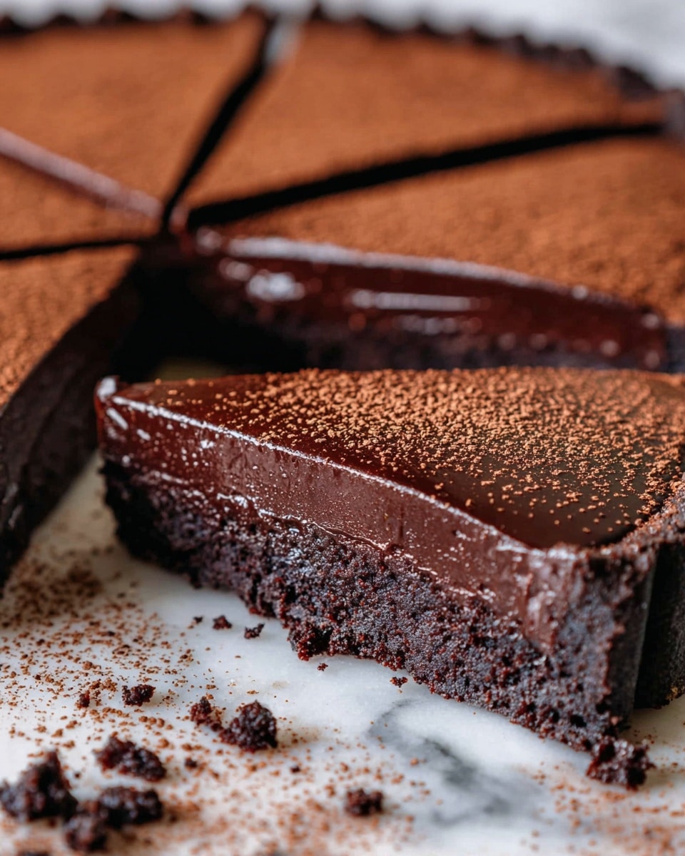 A close-up view of a rich chocolate tart sliced into pieces on a white marbled surface. The tart has two layers: a dense, dark brown crumbly base and a thick, glossy chocolate ganache top layer. The smooth chocolate top is evenly dusted with fine cocoa powder, adding a light brown speckled texture. Crumbs from the base are scattered around the tart, showing its moist and textured nature. The focus is on a single slice slightly pulled away from the rest, revealing the glossy, silky middle layer contrasting with the rough base. photo taken with an iphone --ar 4:5 --v 7