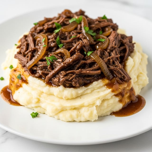 A close-up of a white plate showing a creamy mound of mashed potatoes as the base layer, pale and smooth with slight lumps for texture. On top, there is a thick layer of rich, dark brown shredded beef mixed with caramelized onions, glossy with gravy that spreads slightly onto the potatoes and the plate. Small pieces of fresh green parsley are sprinkled over the meat, adding a pop of color. The plate sits on a white marbled surface. photo taken with an iphone --ar 4:5 --v 7