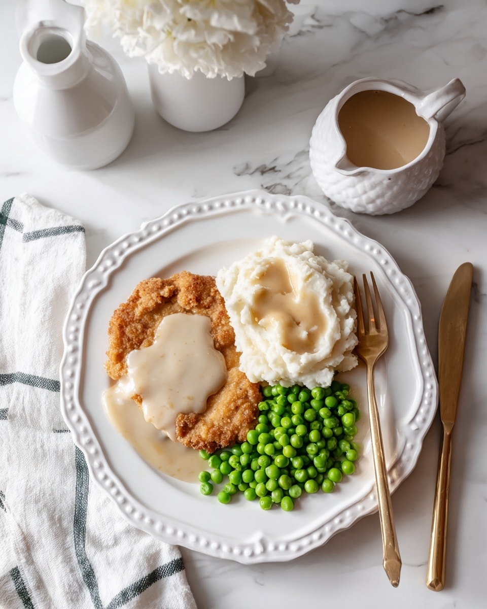 A white scalloped plate holds a serving of three main food parts: a light golden brown fried chicken fried steak covered with a creamy, white gravy on the left side; next to it, at the top right, is a scoop of fluffy, pale mashed potatoes with a smooth pool of white gravy in the center; and at the bottom right is a neat pile of bright green peas. A gold fork rests on the edge of the plate near the peas, and a gold knife is placed above the fried steak with some white gravy on it. The scene is set on a white marbled surface with a white napkin with dark green stripes on the left. In the background, there are white containers and a small white pitcher with some gravy dripping from the lip. photo taken with an iphone --ar 4:5 --v 7
