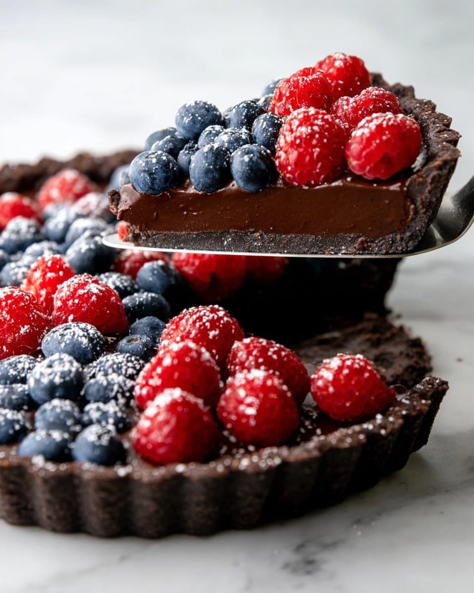 A round tart with three visible layers sits on a white marbled surface: the bottom layer is a dark, crumbly crust; the middle layer is a smooth, glossy dark chocolate filling covering half of the tart; the top layer on the other half is piled with fresh blueberries and raspberries, dusted lightly with powdered sugar. A striped cloth is partially visible near the tart. Photo taken with an iphone --ar 4:5 --v 7