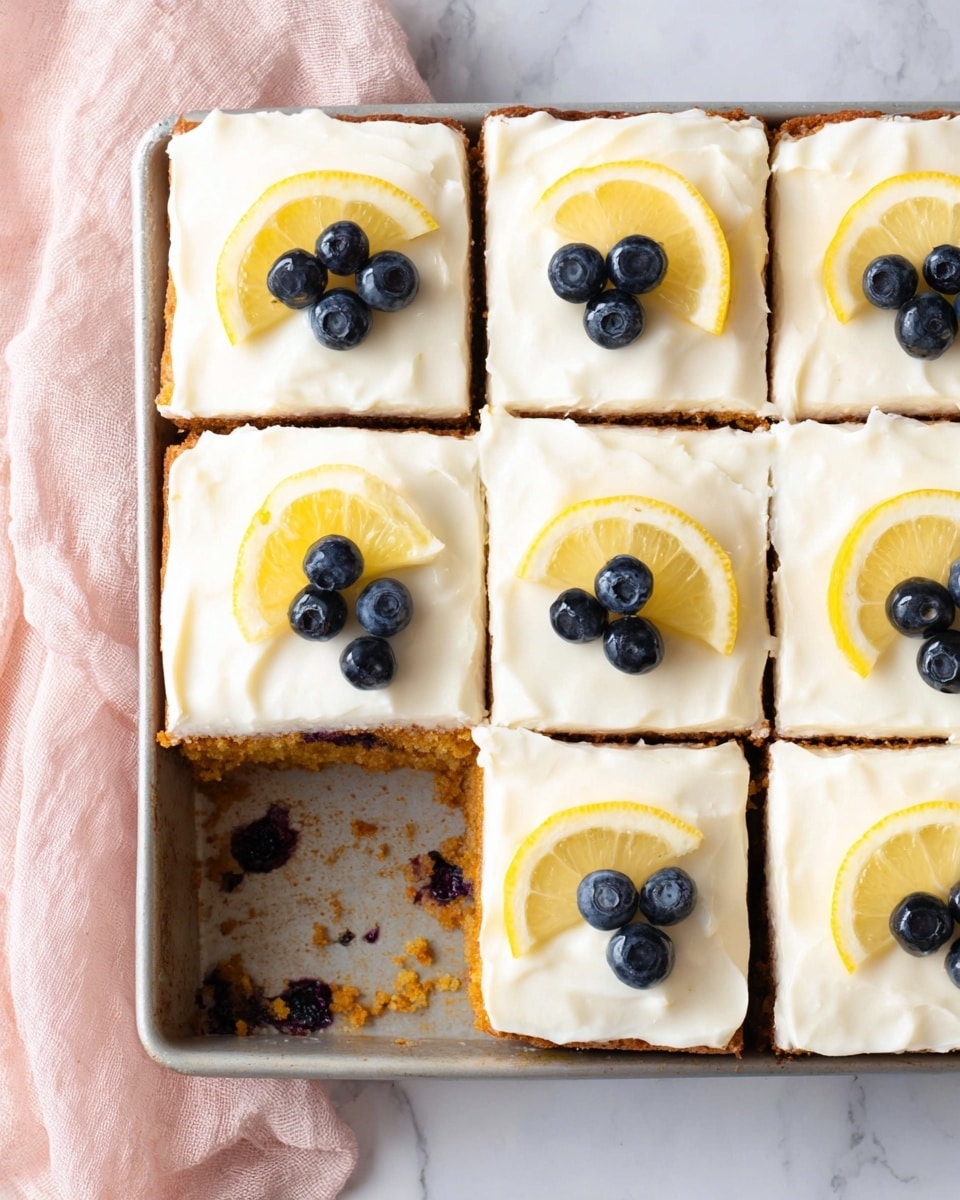 A tray with nine square cake pieces, one piece missing in the bottom left corner showing a golden brown cake base with some dark spots inside, likely blueberries. Each cake square has a thick, smooth layer of white frosting on top. On the frosting, each piece is decorated with a small lemon wedge at the top corner and two blueberries next to it. The tray is on a white marbled surface with a soft pink cloth partially visible on the left side. Photo taken with an iphone --ar 4:5 --v 7