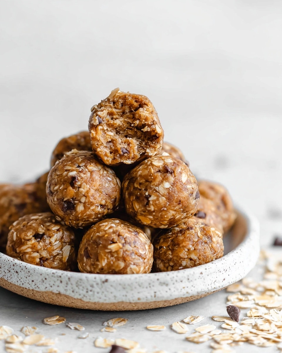 The image shows a tray lined with white parchment paper holding 18 round energy balls arranged in a grid. Each ball is rough-textured with visible oats and small dark chocolate chips mixed inside, giving a light brown and slightly shiny surface. The balls are evenly spaced on a white marbled texture background under soft natural light. photo taken with an iphone --ar 4:5 --v 7