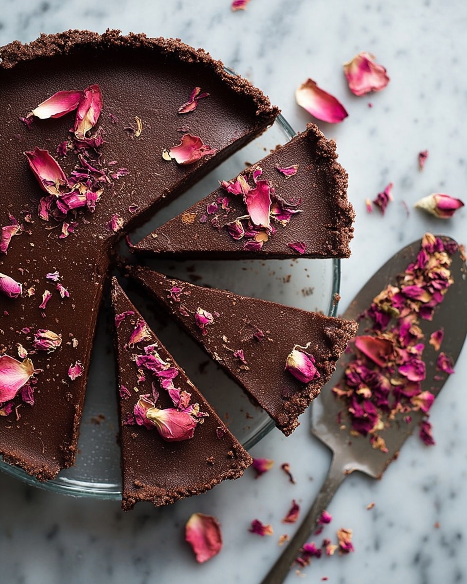 The image shows a chocolate tart cut into six slices, with a smooth, dark brown top layer and a slightly crumbly texture. The tart sits in a clear glass dish on a white marbled surface. Each slice has dried pink rose petals sprinkled on top, adding a delicate and colorful contrast. One slice lies apart on a spatula to the right, also decorated with rose petals. More scattered petals are around the dish, enhancing the visual softness. The surface is a white marbled texture. photo taken with an iphone --ar 4:5 --v 7