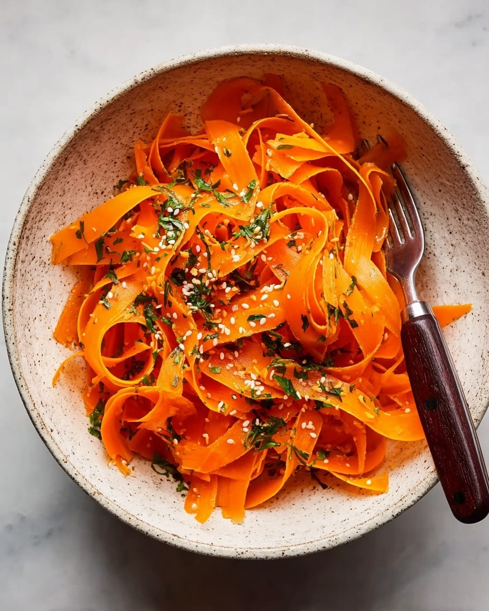 A white speckled bowl holds thin, bright orange carrot ribbons arranged loosely in layers, showing their smooth, curled texture. Small white sesame seeds and finely chopped dark green herbs are sprinkled evenly on top, adding contrast to the vibrant carrots. A dark wooden-handled fork is placed inside the bowl on the right side, partially resting on the carrot ribbons. The bowl sits on a white marbled surface, enhancing the fresh and simple look of the dish. photo taken with an iphone --ar 4:5 --v 7
