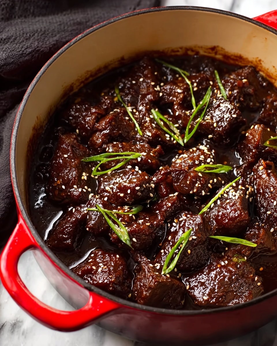 A red pot filled with chunks of dark brown braised meat in a thick, glossy sauce. The meat pieces are textured and coated evenly with the rich sauce, showing tender, slightly caramelized edges. Scattered on top are thin, fresh green onion slices and a light sprinkle of white sesame seeds, adding brightness and contrast. The inside edge of the pot is visible, showing some sauce splashes. The pot sits on a white marbled surface with a blurred dark cloth near the bottom left corner. Photo taken with an iphone --ar 4:5 --v 7