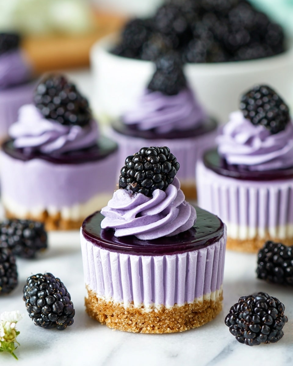 The image shows small purple cheesecakes in white cupcake liners, each having a light brown crumbly crust at the bottom, a thick creamy purple cheesecake layer in the middle, and a glossy dark purple jelly layer on top. A swirl of light purple whipped cream sits above the jelly layer, crowned with a fresh, shiny black blackberry. Additional blackberries are scattered around the cheesecakes on a white marbled surface, and a white bowl filled with blackberries is visible in the background. photo taken with an iphone --ar 4:5 --v 7